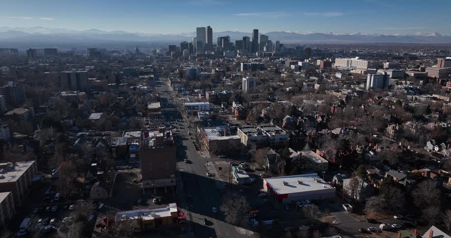 A slow aerial dolly shot reveals the sprawling city of Denver, Colorado, with the downtown skyline and majestic Rocky Mountains on the horizon