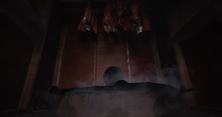 Low angle of thick smoke rising from a fire pit to cure salmon fillets in a traditional smokehouse