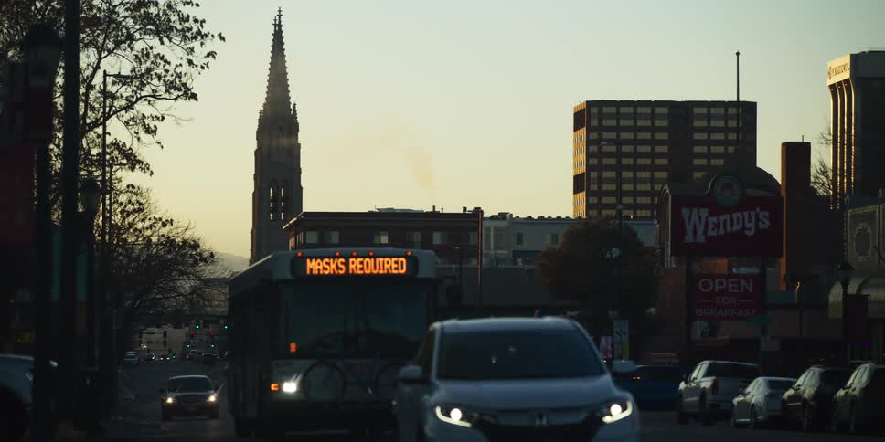 A slow-motion shot of a city street at sunset with traffic and a bus, while a steeple stands tall in the background