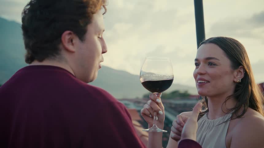 A romantic young couple laughs and talks together while enjoying drinks on a scenic rooftop at sunset