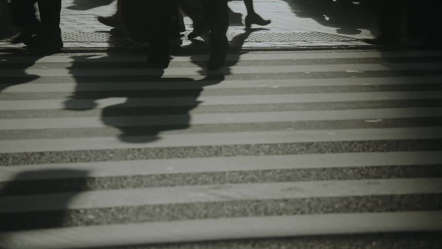 Artistic slow-motion shot of shadows from a crowd of pedestrians crossing a sunlit city crosswalk