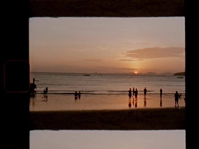 A vintage film-style shot of silhouettes of people enjoying a beautiful sunset on a tranquil beach