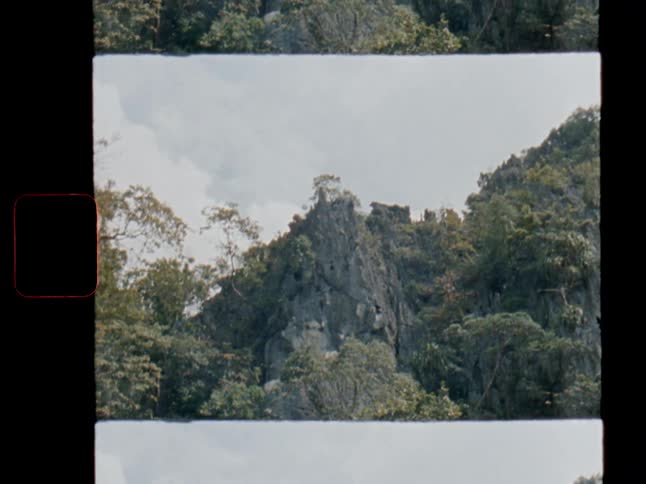 Vintage 8mm film footage reveals a lush, green jungle clinging to a rugged, rocky mountainside