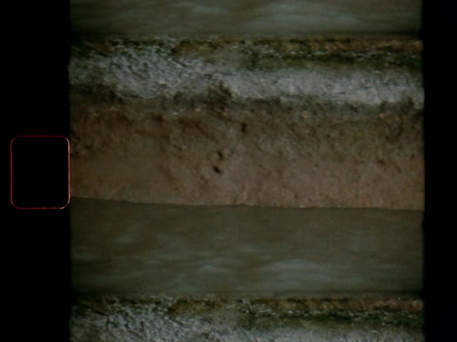 An archival film shot captures a close-up of muddy water flowing through geological soil layers