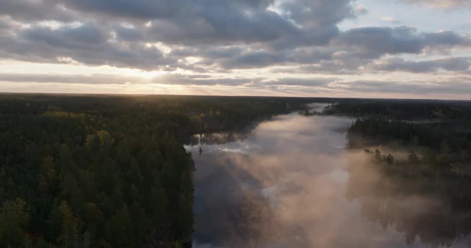 An ethereal aerial view shows a golden sunrise over a misty lake surrounded by a vast forest