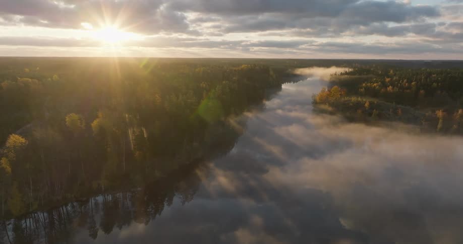 An ethereal aerial shot captures the sunrise casting golden light and long shadows over a misty, forested river valley