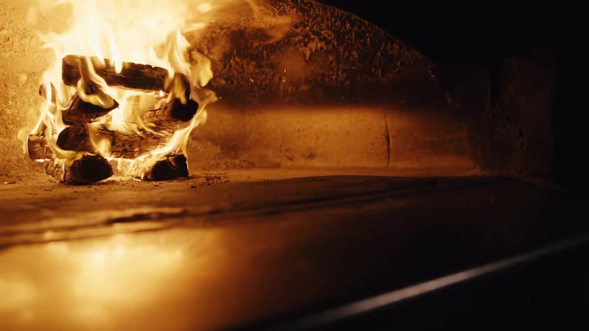 A stack of wood burns brightly inside a traditional stone pizza oven, casting a warm and inviting glow