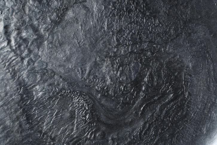 Hypnotic swirls of dark, glittery metallic paint create an abstract, textured background