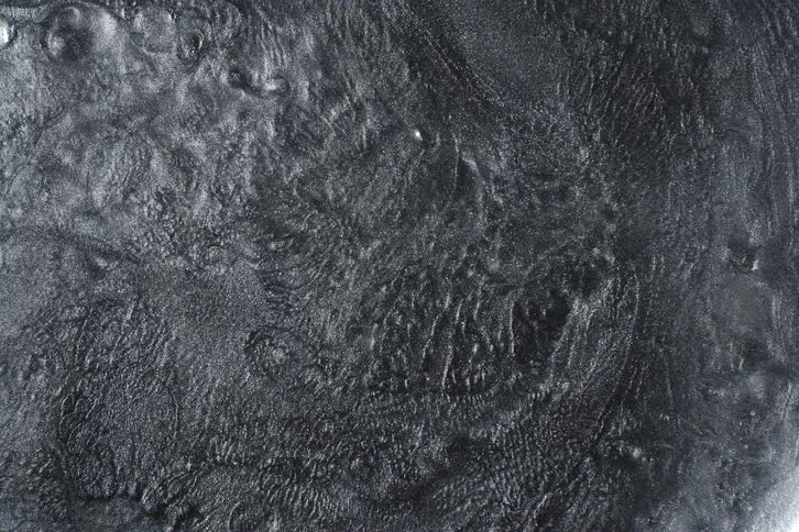 A mesmerizing overhead view of a slowly churning, dark, viscous liquid with a metallic sheen