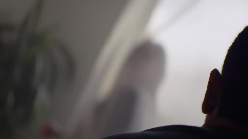 Moody, blurry shot from behind a silhouetted person wearing red headphones looking out a window
