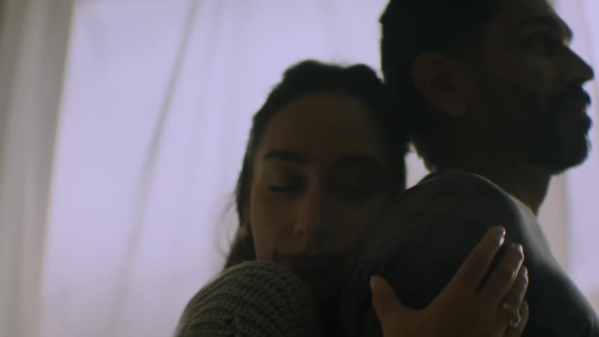 A thoughtful couple shares a quiet and intimate embrace while silhouetted against a window
