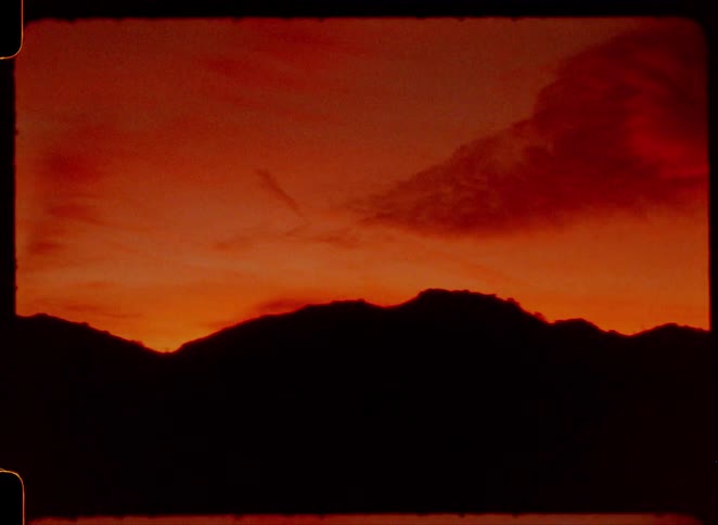 Super 8 footage of a dramatic fiery red sunset timelapse over silhouetted mountains