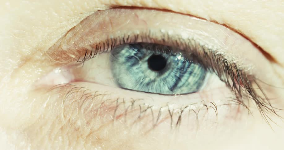 A dramatic macro shot captures a striking blue eye opening slowly, with the pupil dilating as the light fades