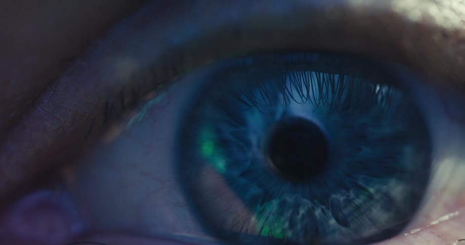 An extreme close-up macro shot of a blue human eye as light slowly illuminates its intricate iris and pupil