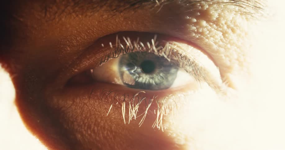 A dramatic macro shot of a blue human eye slowly opening, with its eyelashes catching the bright, intense light