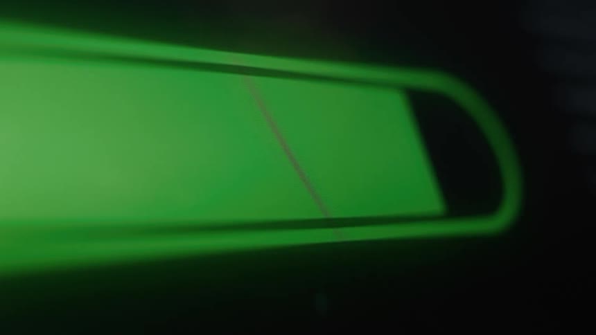 Abstract macro shot of a glowing green battery indicator charging on a dark background