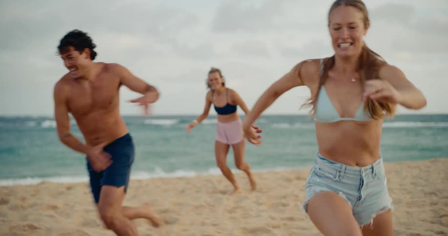 A group of young friends joyfully play a game of soccer on the beach together in slow motion