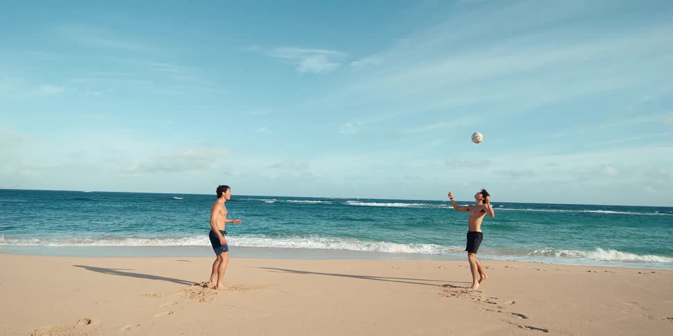 A cinemagraph shows two men playing volleyball on a sunny tropical beach as the ball hangs in the air