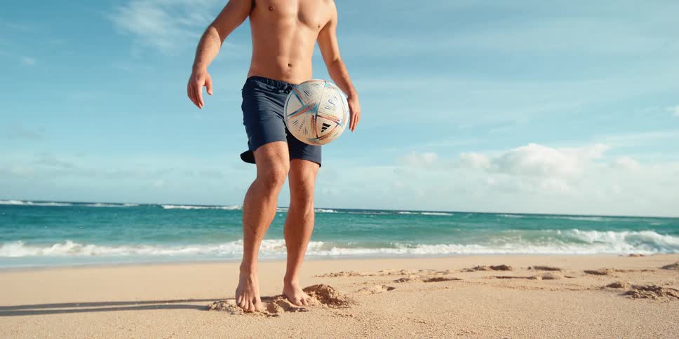 A man juggles a soccer ball with his feet and knees on a sandy beach in super slow motion