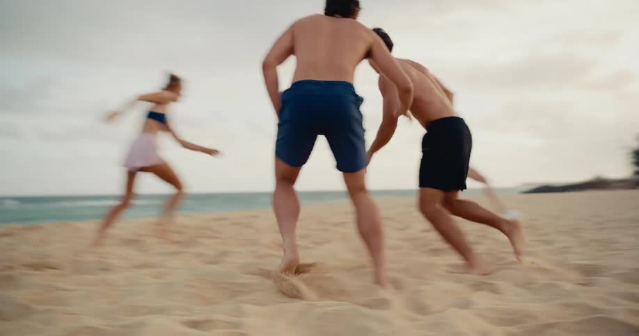 A group of energetic young friends run barefoot and compete in a fun game of soccer on a beautiful sandy beach