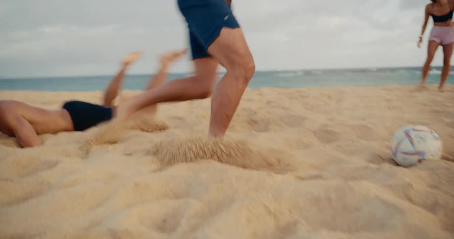 Athletic young friends have a competitive game of soccer on a sandy beach at dusk