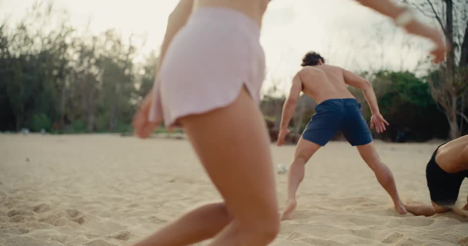 A group of active friends enjoys a competitive game of soccer on the beach, kicking up sand in slow motion