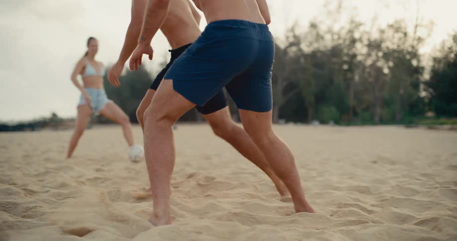 Close-up slow motion shot of athletic friends playing a fun game of soccer barefoot in the sand on the beach