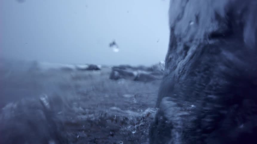 A super slow motion close-up of turbulent water splashing against a rock and freezing into a solid sheet of ice