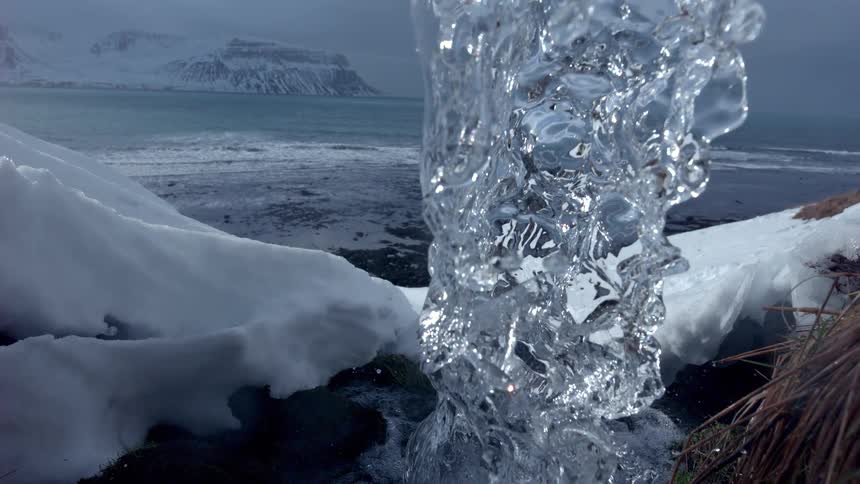Super slow motion closeup of a crystal clear waterfall flowing over a snowy bank towards the ocean in Iceland
