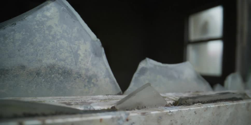 Slow pan across the broken and grimy window of a derelict and forgotten building