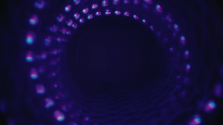 A slow journey through an abstract, spiraling tunnel of colorful glowing lights that fade into darkness