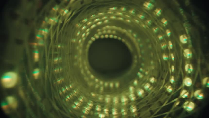 Camera slowly pulls back out of a dark, abstract tunnel illuminated by swirling green LED lights