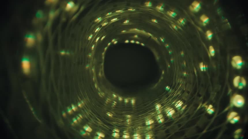 Slowly moving through a glowing, abstract tunnel made of a coil of green and yellow LED lights