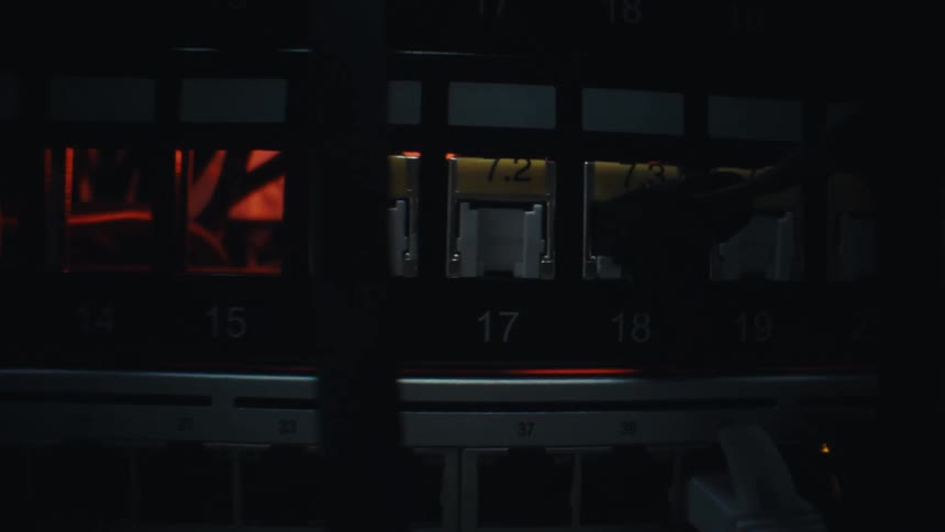 A slow dolly shot pushes into a dark server room rack focusing on the blinking lights and ethernet ports of the network switch