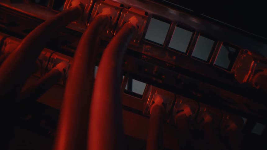 A close-up camera move along bundled ethernet cables leads to a server rack in a dark data center illuminated by intense red light