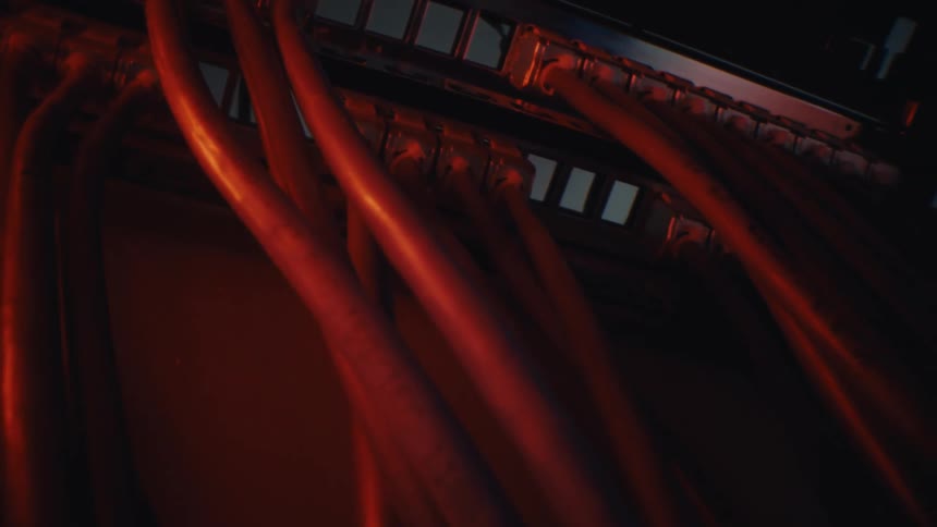 A macro dolly shot reveals a network switch with plugged-in ethernet cables in a server room with ominous red lighting