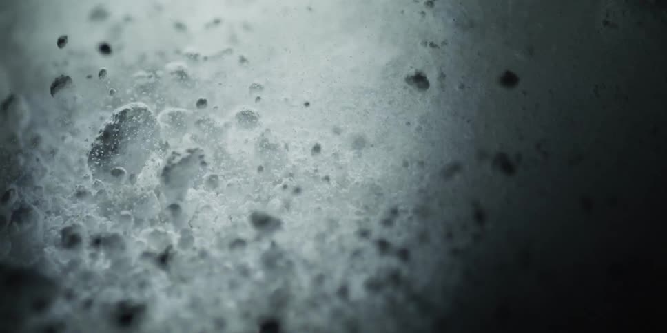 Slow pan across a dark, abstract, and textured surface reminiscent of a lunar landscape in extreme close-up