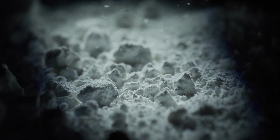 A light source slowly illuminates white powder in the darkness, creating a moody and abstract scene in slow motion