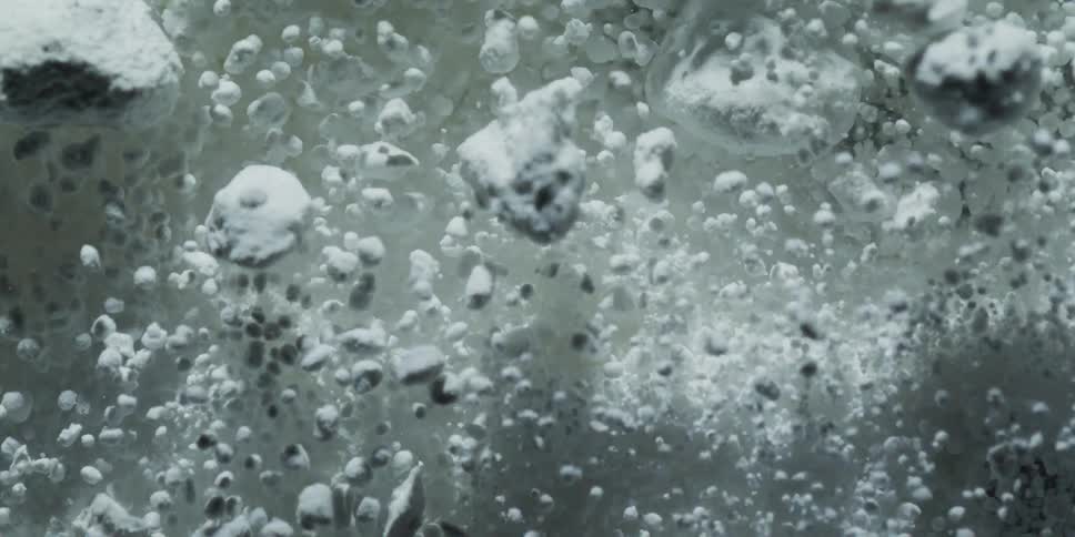 Macro shot of a chemical reaction as white porous particles bubble and rise in dark liquid