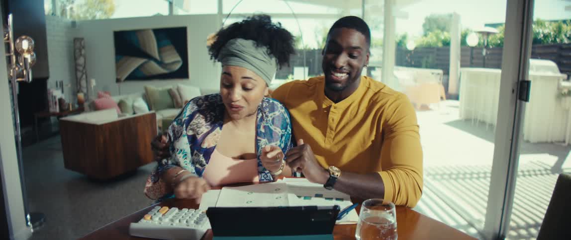 An excited young couple gets great news while doing their finances together in their modern, sunlit home, filmed in slow motion