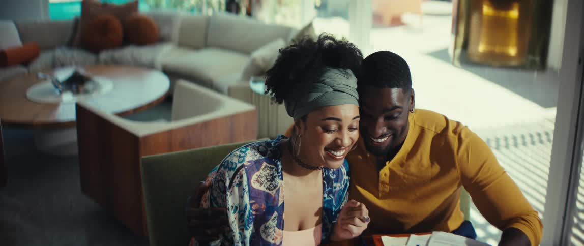 A happy young couple laughs with joy while reviewing their finances at the dining table in their modern home