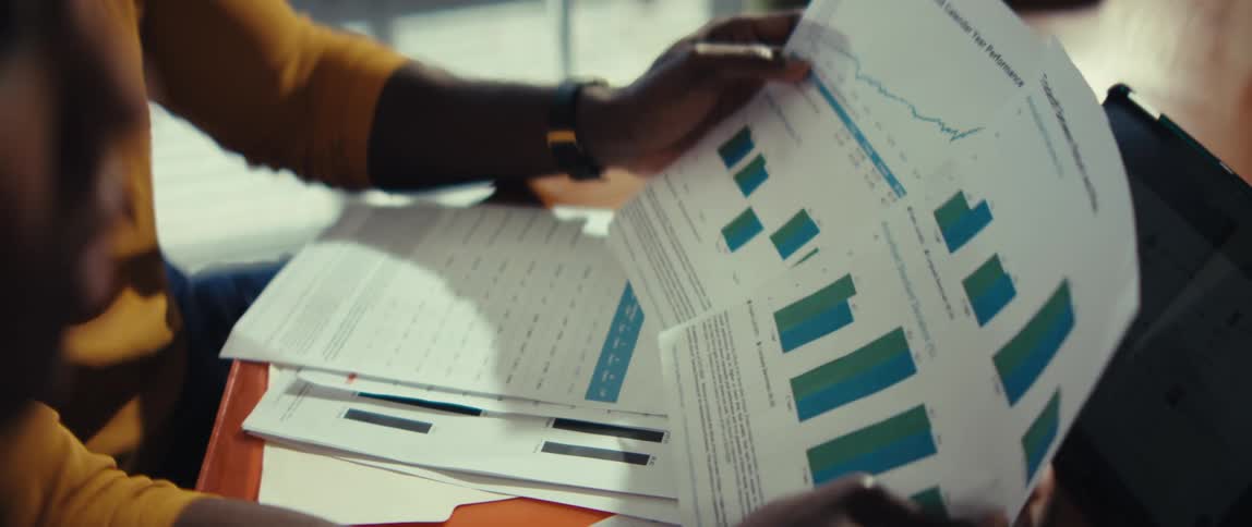 Over-the-shoulder close-up of two diverse colleagues analyzing financial charts and graphs during a business meeting