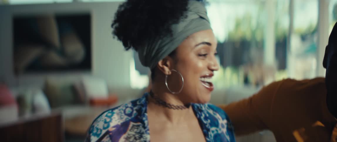Close up of an expressive young woman with a headwrap smiling and talking with friends in her bright living room