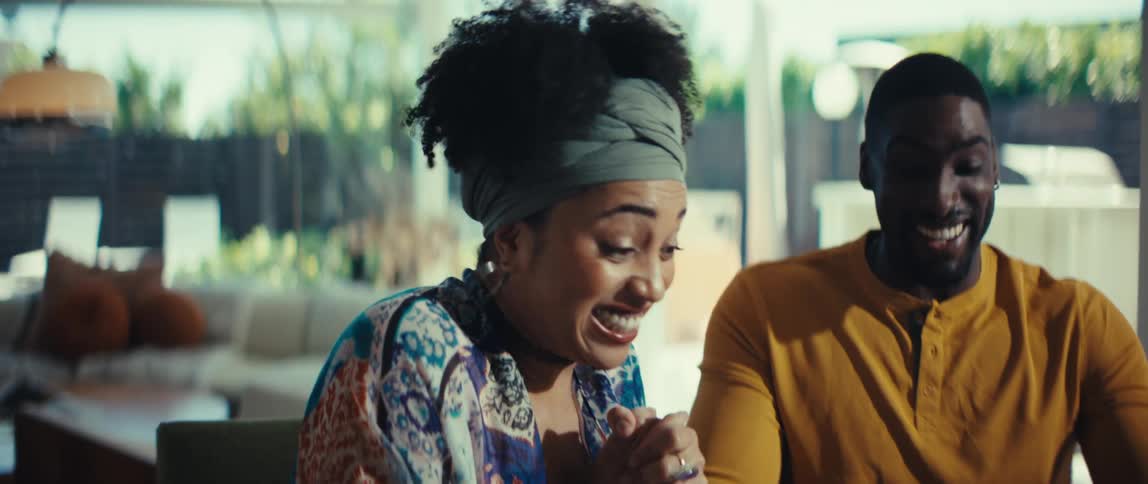 A happy African American couple sits at their dining room table and reacts with joy and excitement to good news while doing their taxes in slow motion