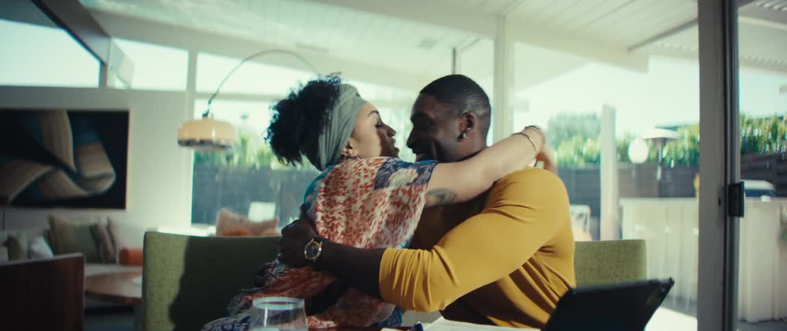 A stylish young couple celebrates a success, sharing a happy hug and kiss in their sunlit modern home