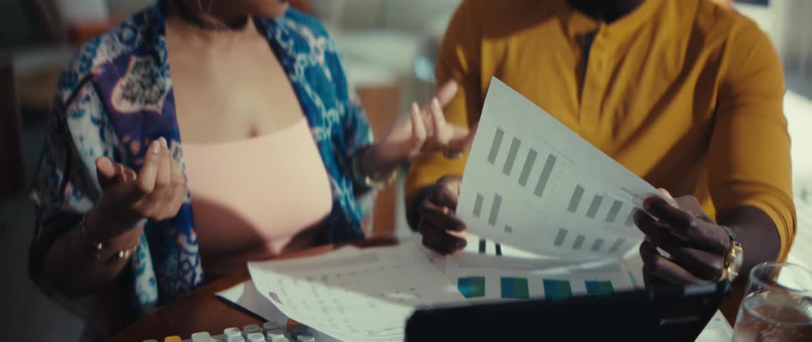 A young couple has a serious and stressful discussion while reviewing financial charts and paperwork at their dining table