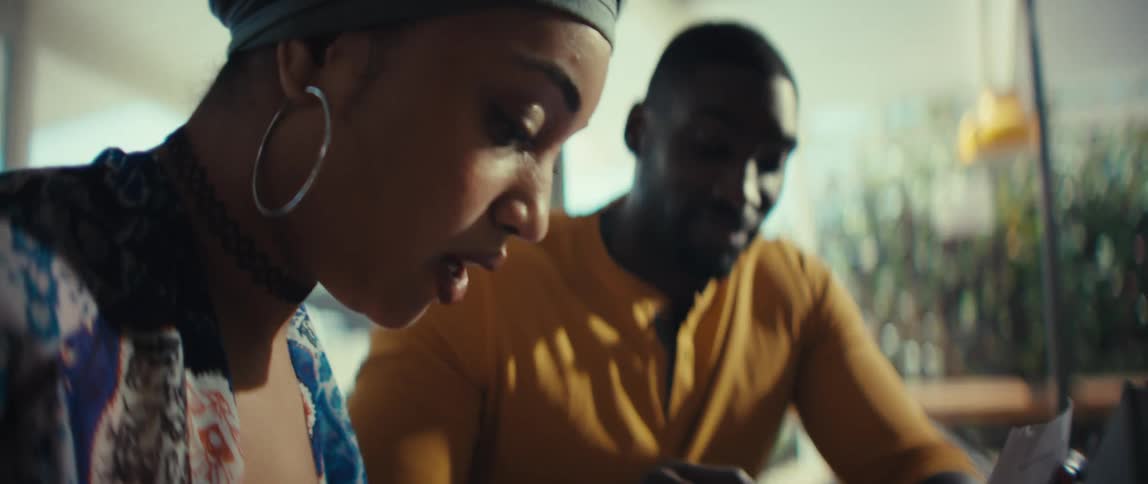 A slow-motion close-up shot focuses on a young Black couple as they collaborate on managing their finances at home