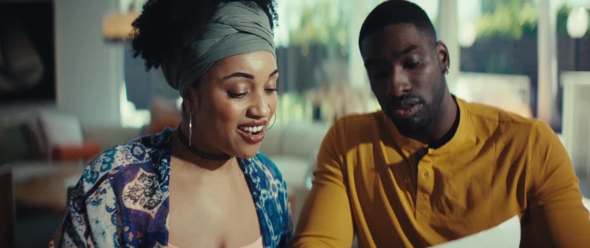A young African American couple happily review bills and documents together at home, smiling and laughing at the good news