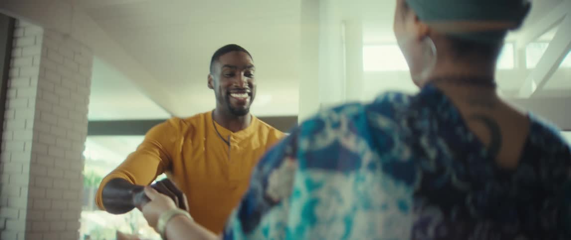 A young romantic couple smiles and laughs while slow dancing together in their bright and sunny living room