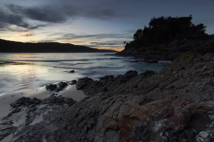 A stunning timelapse captures the changing light and rising tide along a rugged, rocky coastline as day transitions into night